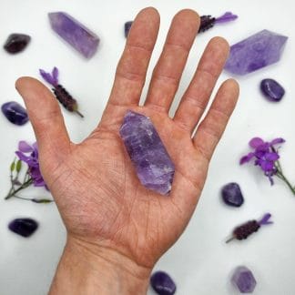 amethyst double point 26-50g in hand with crystals in background