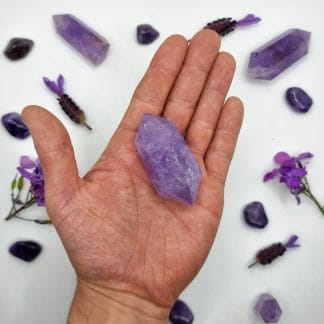 amethyst double point 51-75g on hand with crystals in background